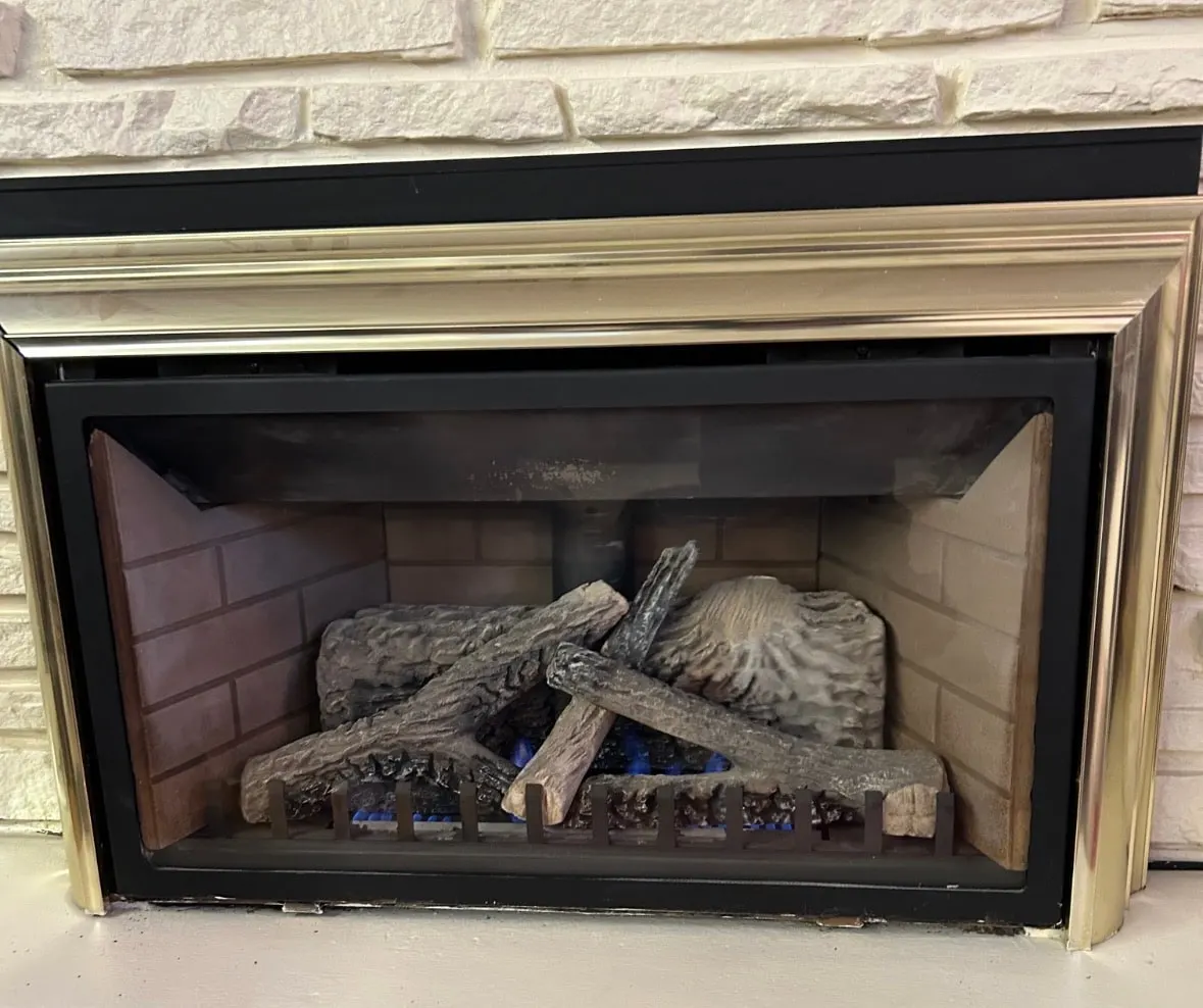 Lit gas fireplace with ceramic logs set into a white brick wall