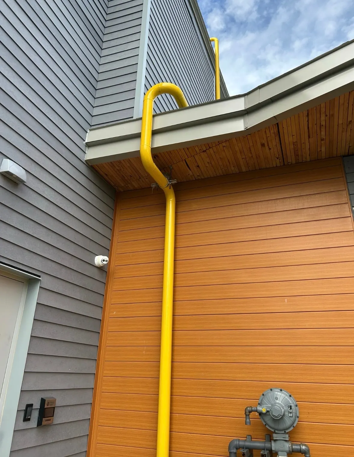 Yellow natural gas riser running down an exterior wall to the gas meter and regulator
