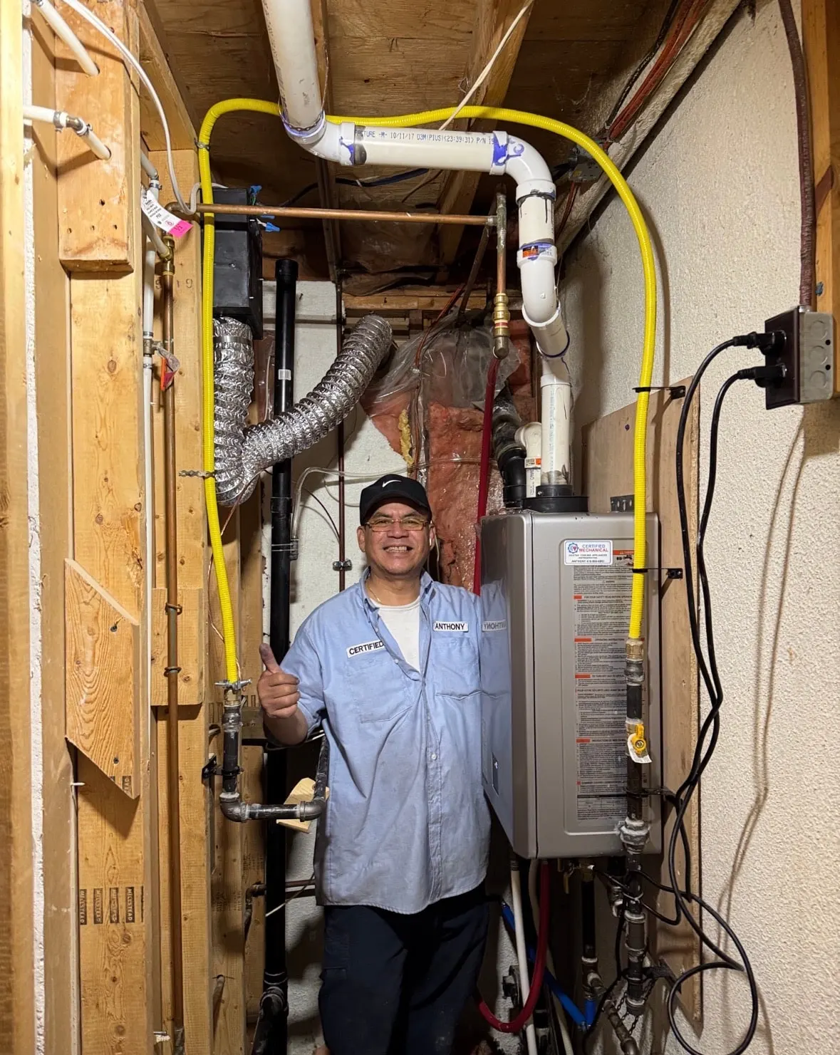Certified Mechanical technician in uniform beside a gas tankless water heater and its yellow gas line in a basement